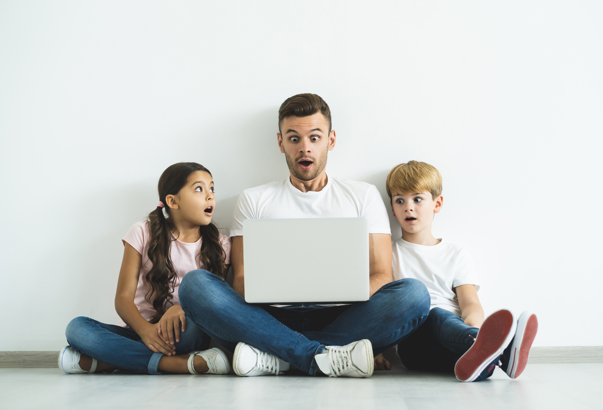 The surprised father and children with a laptop sitting on the floor