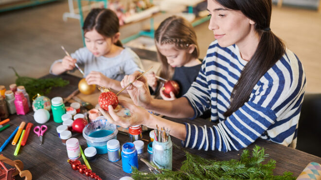 Woman making Christmas decorations sitting at table with two little girls