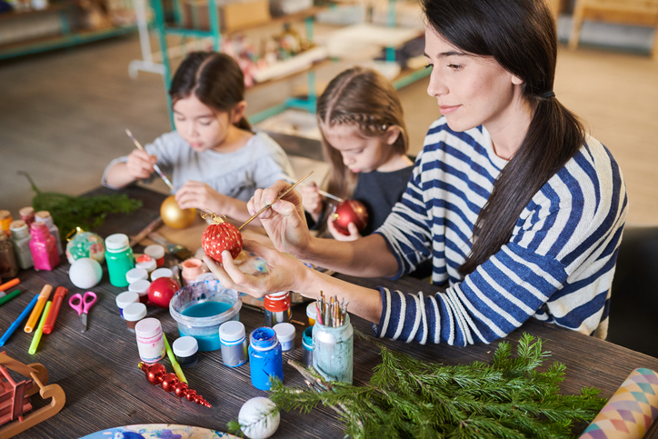 Woman making Christmas decorations sitting at table with two little girls