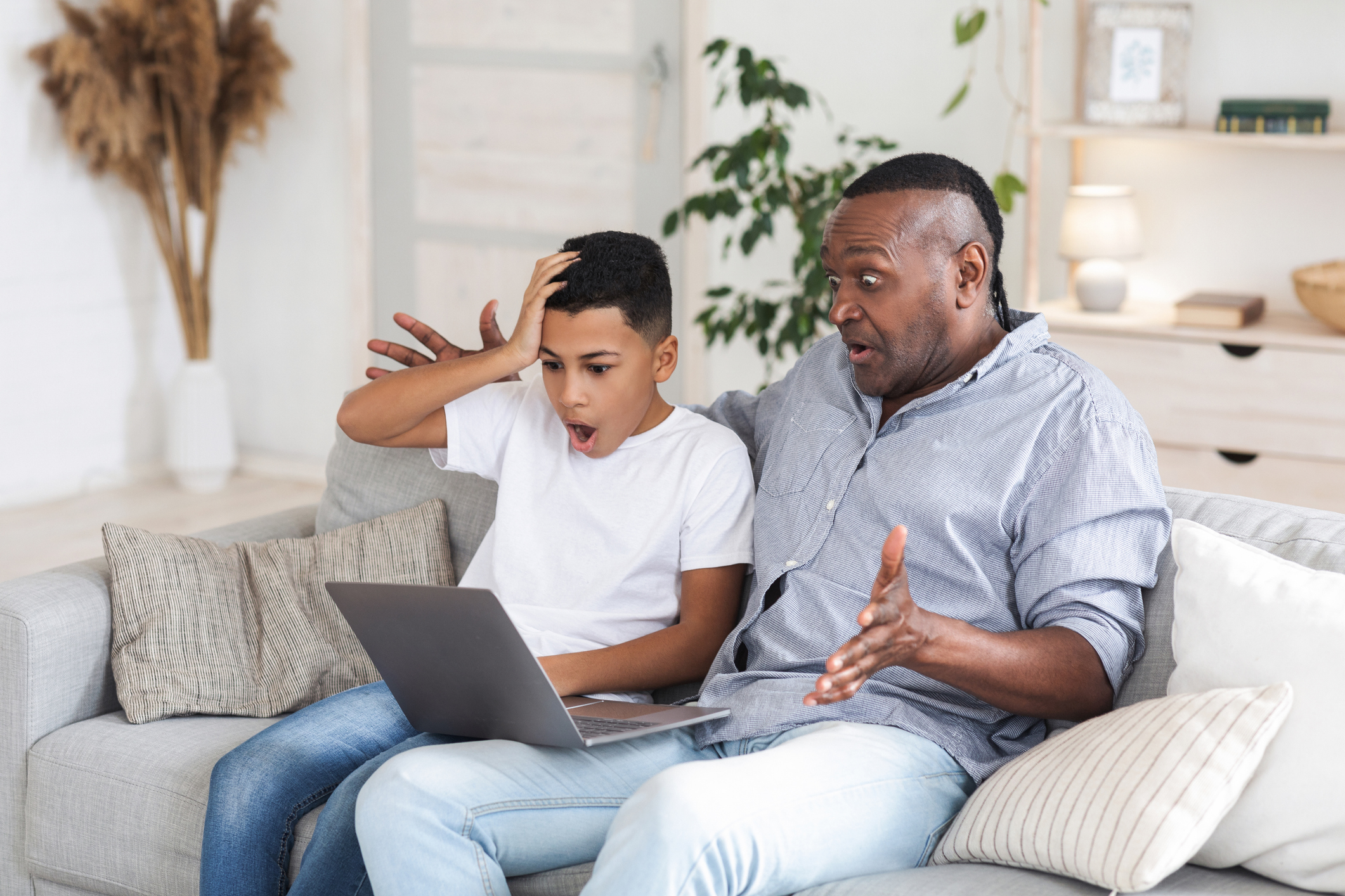 African boy and his grandfather looking at laptop screen with shock