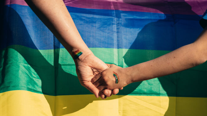 Mom and daughter holding hands in front of a pride flag