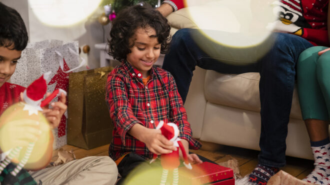 Shot of a family with two sons opening Christmas presents on Christmas morning in the Northeast of England. Their parents are sitting on the sofa watching the children unwrap their gifts.