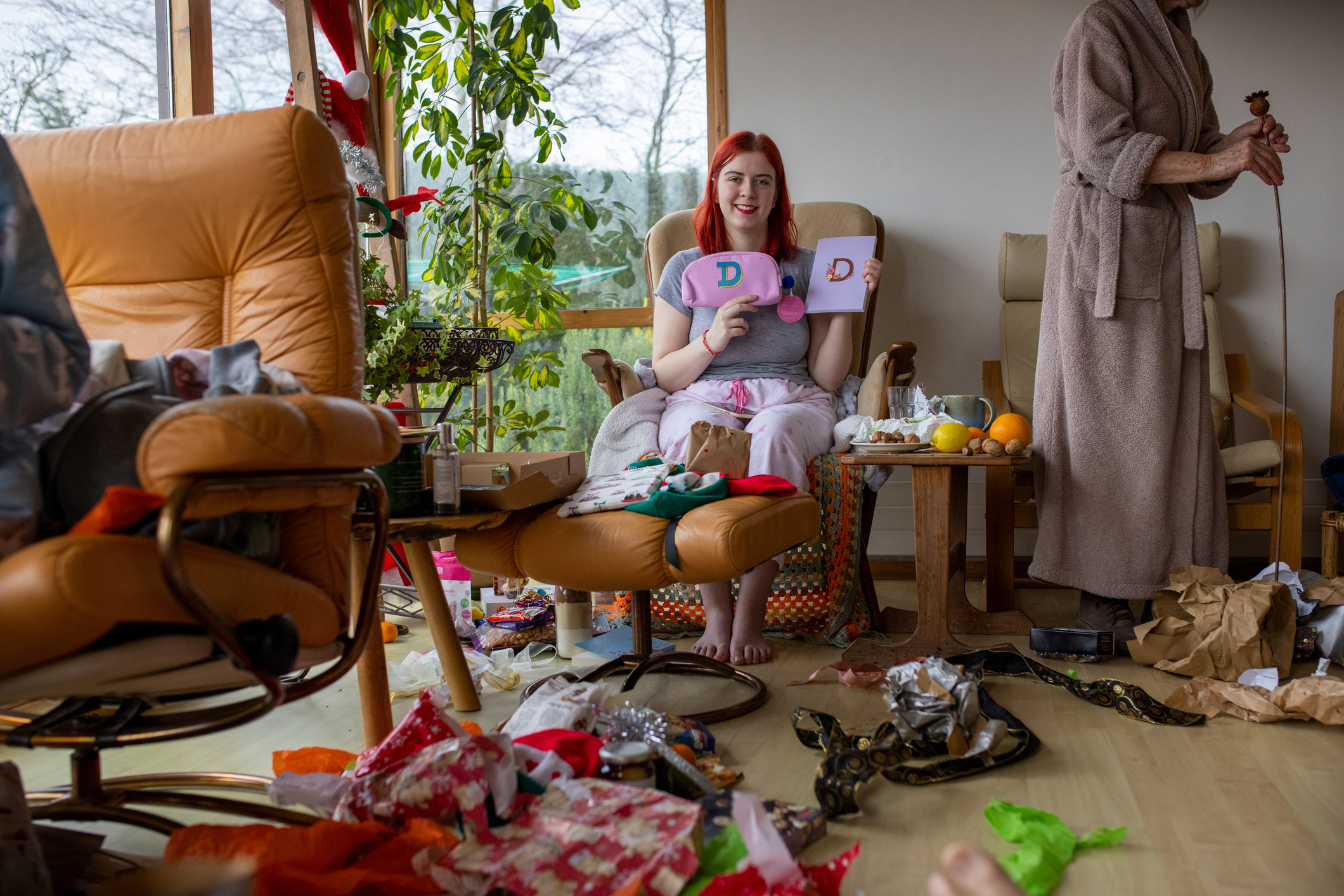 A teenager with vibrant dyed red hair with her grandmother in their living room in their home in Hexham, Northumberland in the North East of England. She is looking and smiling at the camera as she holds a new diary and pencil case which she has been gifted for Christmas.