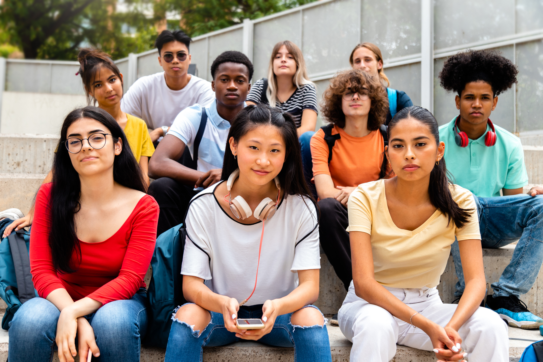 Group of multiracial teen high school students looking at camera sit on stairs outdoors.