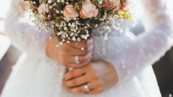 A bride stands in a white dress, cradling a bouquet of freshly-cut flowers