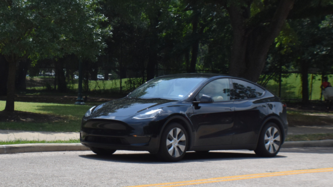 black Tesla driving down a tree-lined street