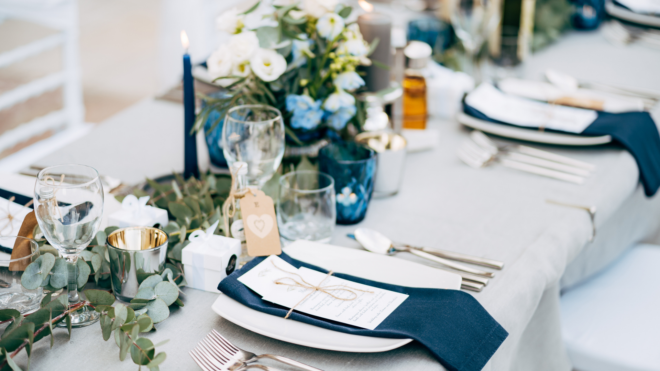 a wedding reception table set with plates, utensils, napkins, glasses, menus and flowers