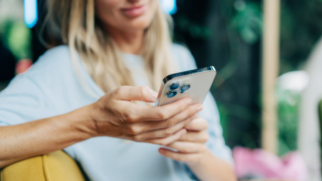 woman with blonde hair sitting outside and looking down at a phone